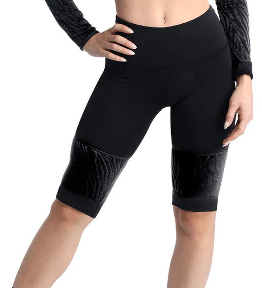 Dancer is wearing black, high waisted, knee length, bike shorts with zebra pattered mesh panels. She has paired the garment with a matching long sleeve top and has her right hand at her hip.