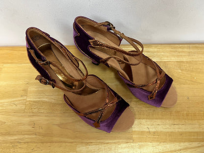 A  pair of Latin ballroom shoes with a 2" flared heel featuring a purple velvet vamp and heel with bronze trim. Side double buckle closure.