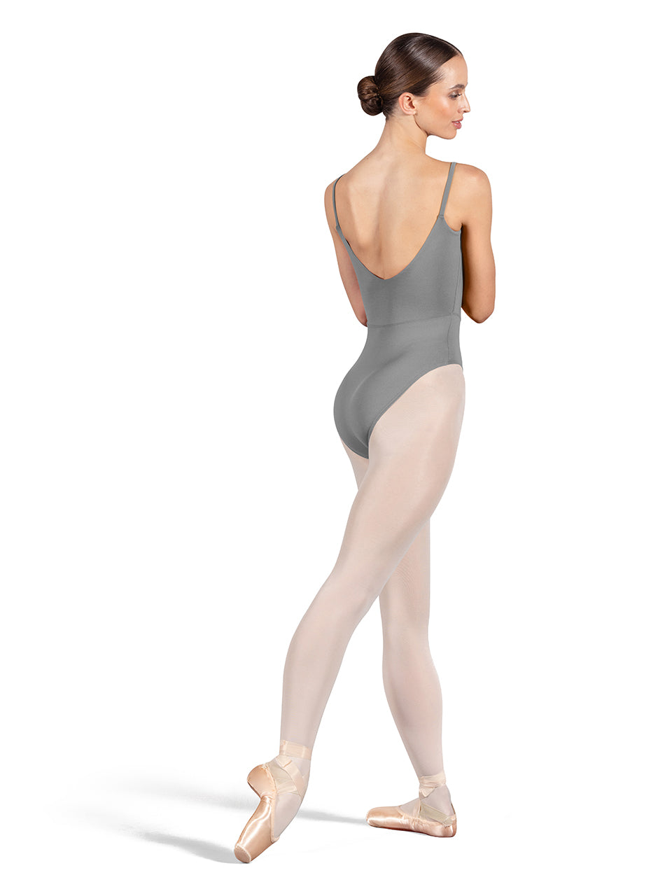 Dancer is wearing a gray, camisole leotard with a scoop neck and back and bodice seam detail. She has paired the garment with pink tights and pointe shoes. Dancer is standing with her right foot pointed back and is showing a back angle of the leotard.