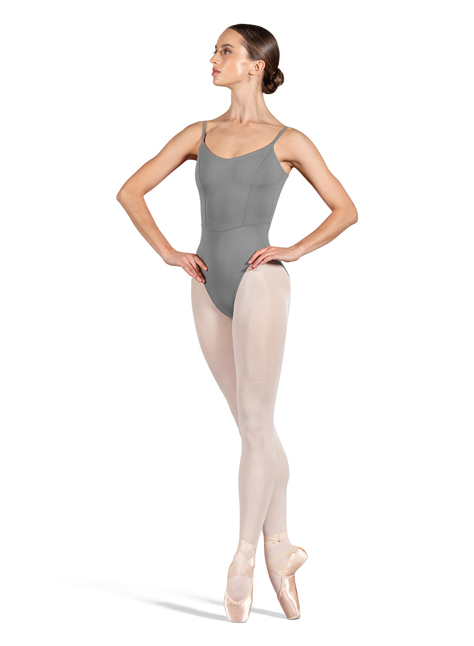 Dancer is wearing a gray, camisole leotard with a scoop neck and back and bodice seam detail. She has paired the garment with pink tights and pointe shoes and is balancing in a fourth position releve on pointe with her hands on her hips.