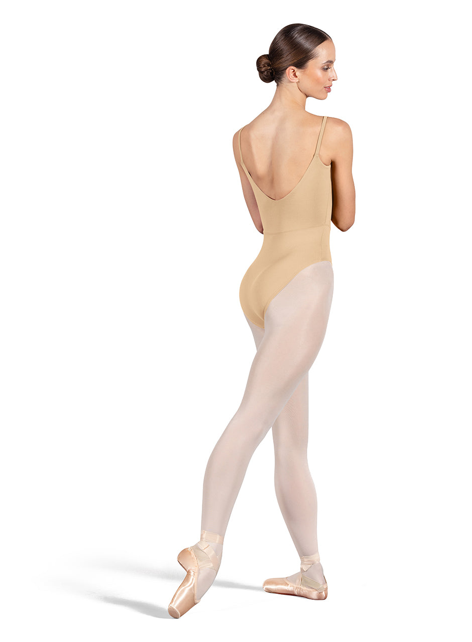 Dancer is wearing a sand, camisole leotard with a scoop neck and back and bodice seam detail. She has paired the garment with pink tights and pointe shoes. Dancer is standing with her right foot pointed back and is showing a back angle of the leotard.