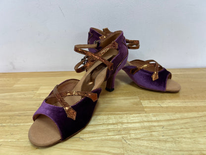 A  pair of Latin ballroom shoes with a 2" flared heel featuring a purple velvet vamp and heel with bronze trim. Side double buckle closure.