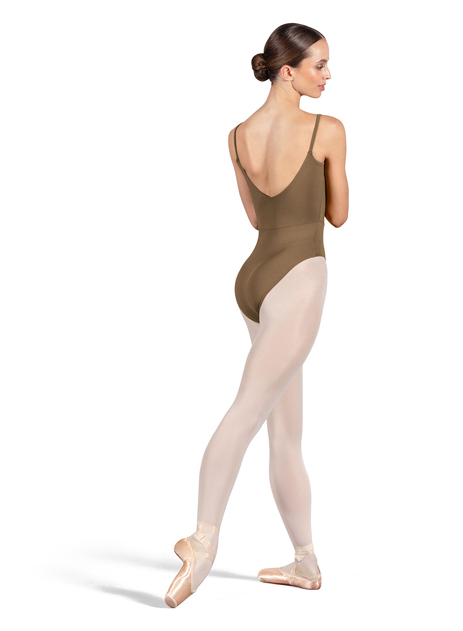 Dancer is wearing an almond, camisole leotard with a scoop neck and back and bodice seam detail. She has paired the garment with pink tights and pointe shoes. Dancer is standing with her right foot pointed back and is showing a back angle of the leotard.