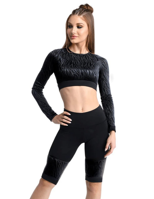 Dancer is wearing black, high waisted, knee length, bike shorts  with zebra pattered mesh panels. She has paired the garment with a matching long sleeve, mid rise top and has her right hand at her hip.