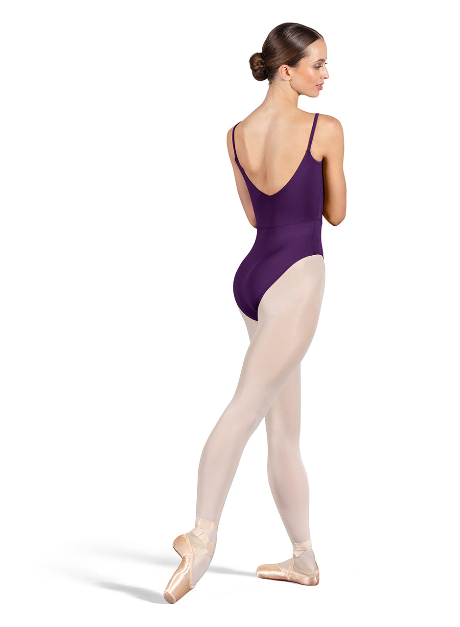 Dancer is wearing an aubergine, camisole leotard with a scoop neck and back and bodice seam detail. She has paired the garment with pink tights and pointe shoes. Dancer is standing with her right foot pointed back and is showing a back angle of the leotard.