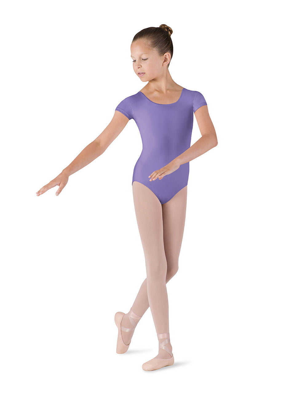 Dancer is wearing a lavender, cap sleeve, scoop neck leotard. She has paired the garment with pink tights and ballet shoes with ribbons tied around the ankle. Dancer is standing in a B+ position with her left foot back and hands reaching to the right side of her body.